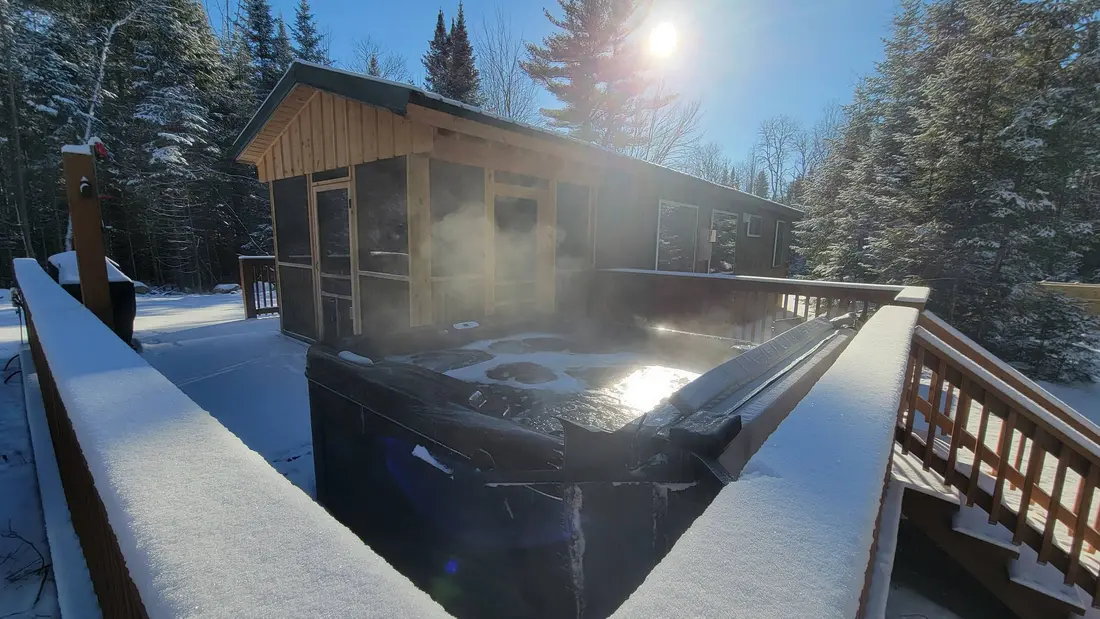 The hot tub steaming on The Modern Pine's deck on a cold, clear morning, with the screened room behind it